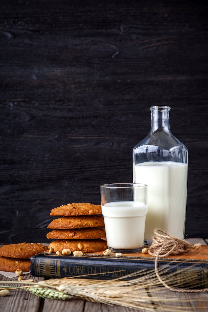 Glass of milk with stack of cookies, book, and bottle on a rustic wooden table.